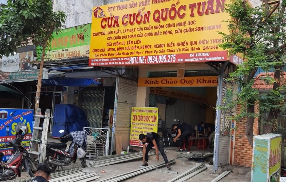 Cửa hàng Cửa Cuốn Quốc Tuấn, thợ đang xếp lá cửa cuốn ngay trước mặt tiền
