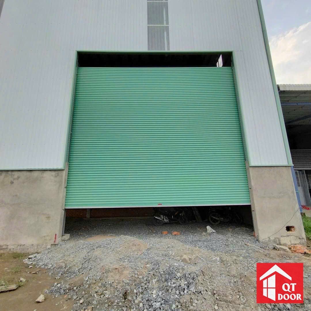 Cửa cuốn màu xanh ngọc khổ lớn Quốc Tuấn lắp ở nhà xưởng vách tôn trắng, cửa kéo lên một phần